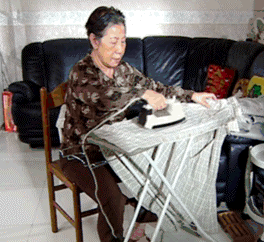 In the picture, an elder is sitting on a chair and ironing the clothes.