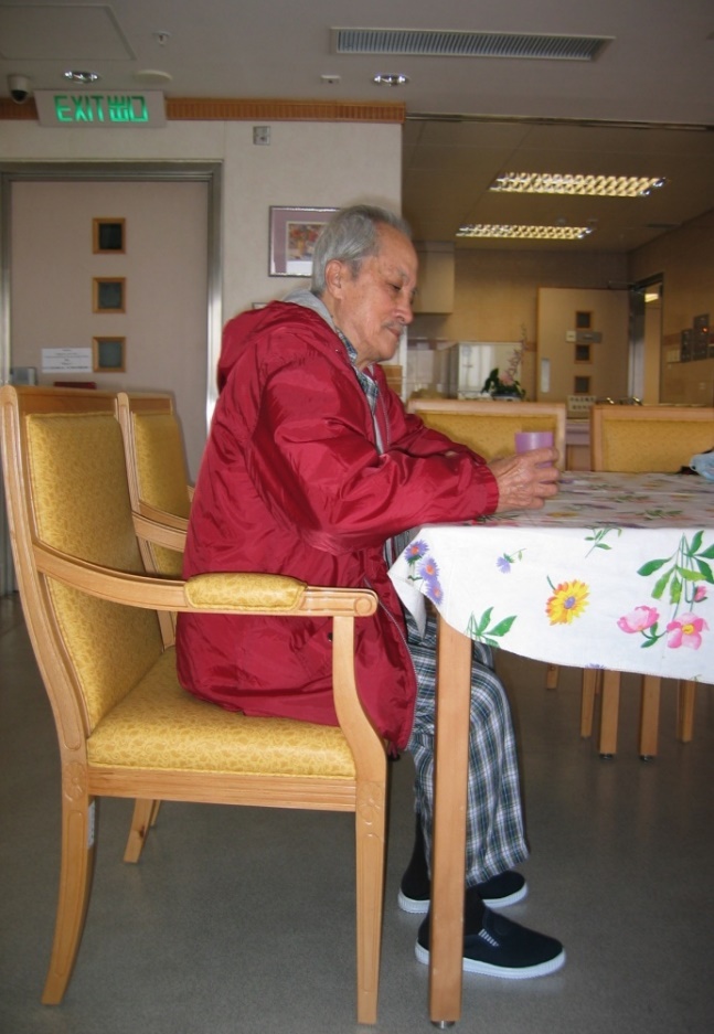 The diagram shows an elderly male holding a cup in sitting position at the table. 
The height of the table is appropriate for him so as to allow his forearm to be placed over the table comfortably 