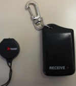 图二： 图中显示一个防走失警报器，它有两部份，一个可挂在颈上的黑色圆形装置传感器, 及 一个可扣在身上黑色方形装置显示器