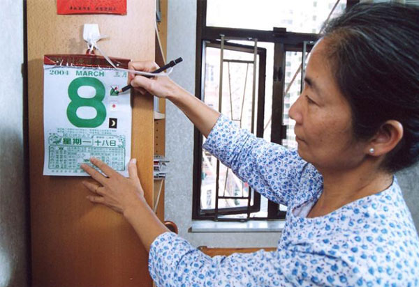 一名女士在家中用笔在中式日历上做记号