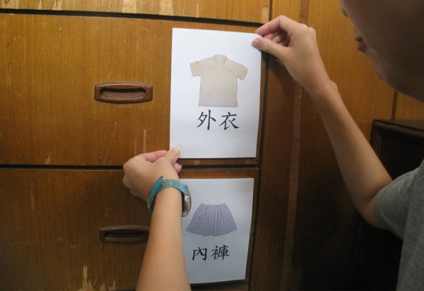 一個有多個抽屜的衣櫃，其中一個貼有寫上「外衣」和外衣照片的標示，另一個貼有「內褲」和內褲照片的標示