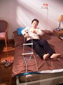 圖中顯示一位長者抓緊床尾繩梯，一步一步借力起床