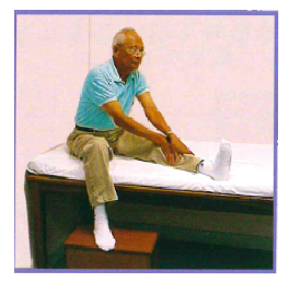 圖二:腿後肌肉伸展運動 長者坐在床邊,左腿伸直放在床上,右腿曲膝沿床邊放下,腳踏矮櫈或地上。長者腰背挺直及左膝伸直,雙手放於脛上,向腳尖方向推前